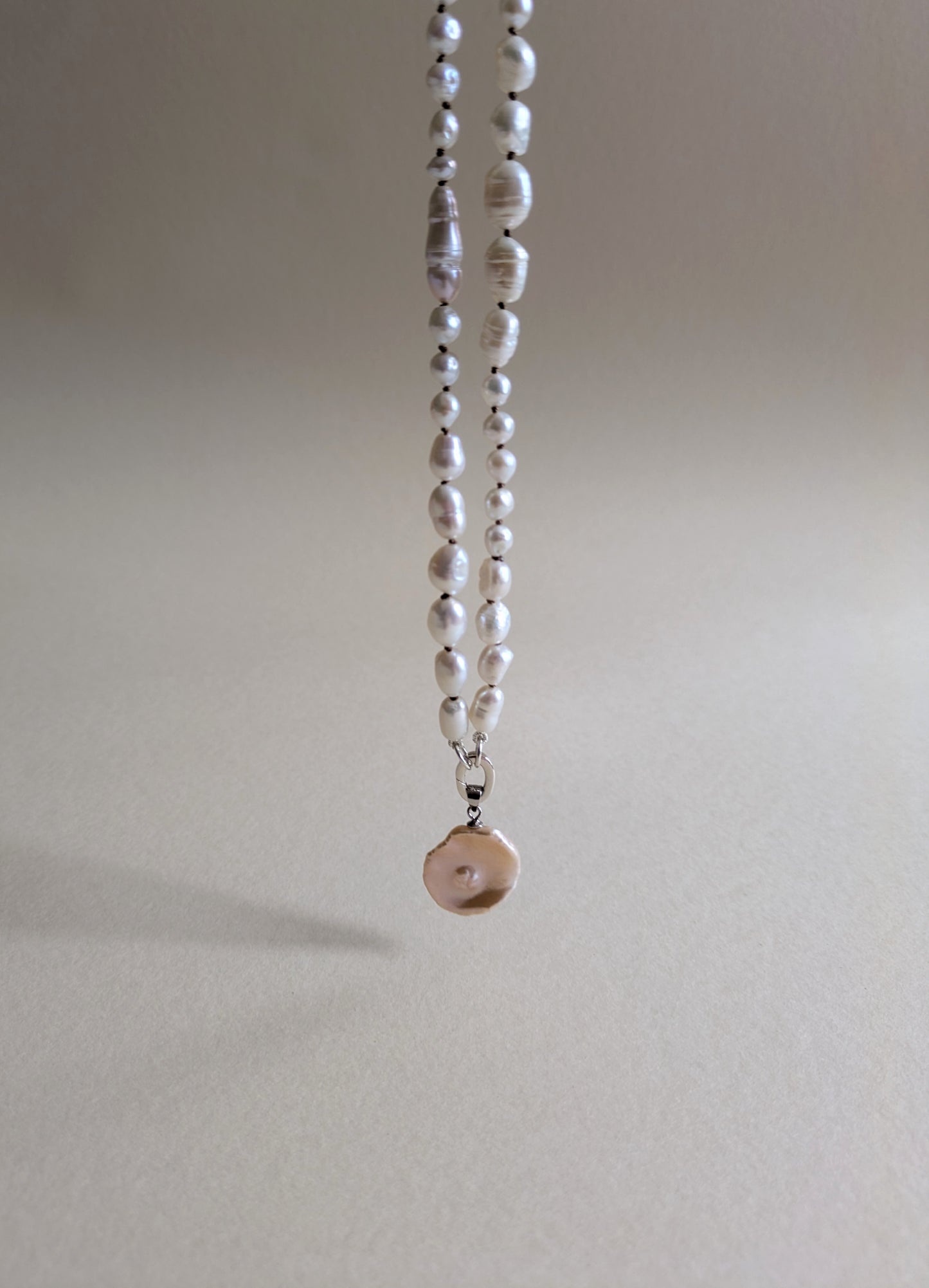 Pearl necklace with a pendant on a plain background