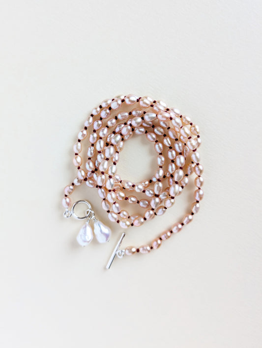 Details of a long pink rice pearl necklace with silver clasp.
