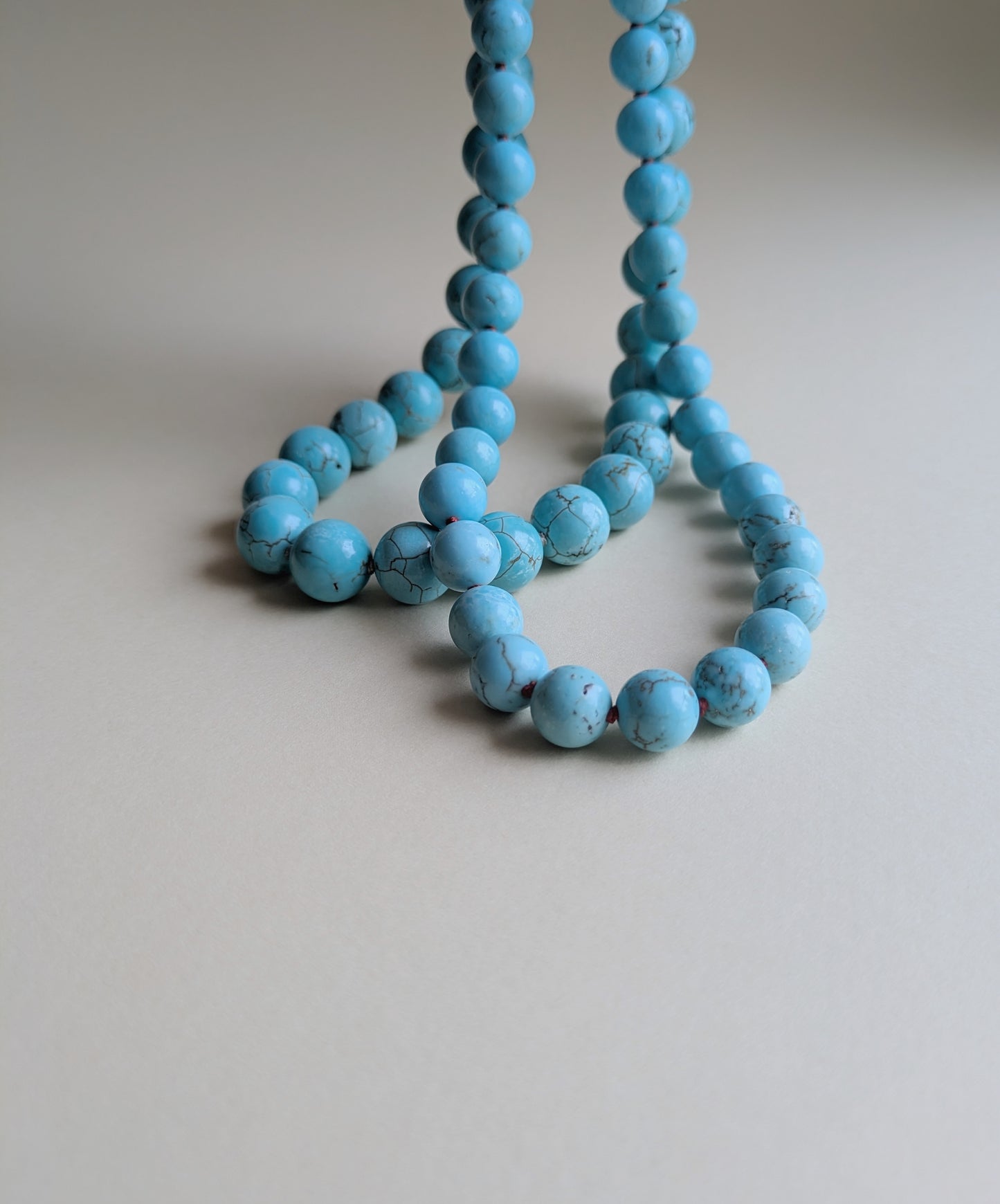A strand of turquoise blue round beads, likely a necklace or bracelet, draped on a neutral light gray background.