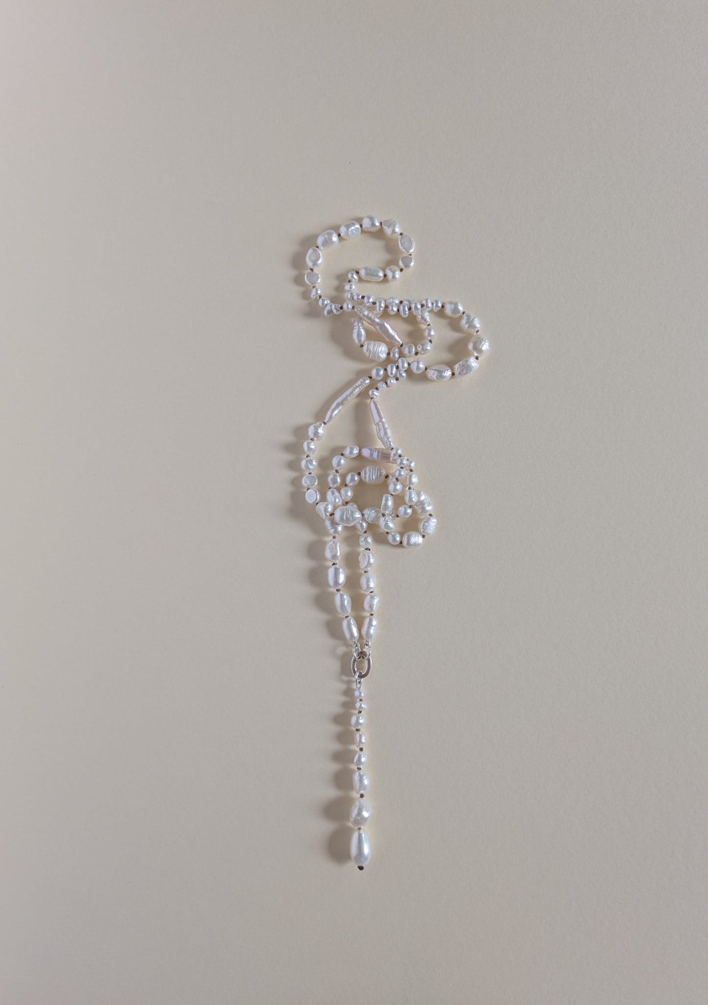 A delicate white beaded necklace with a long, ornate drop pendant, laid flat on a solid beige background.