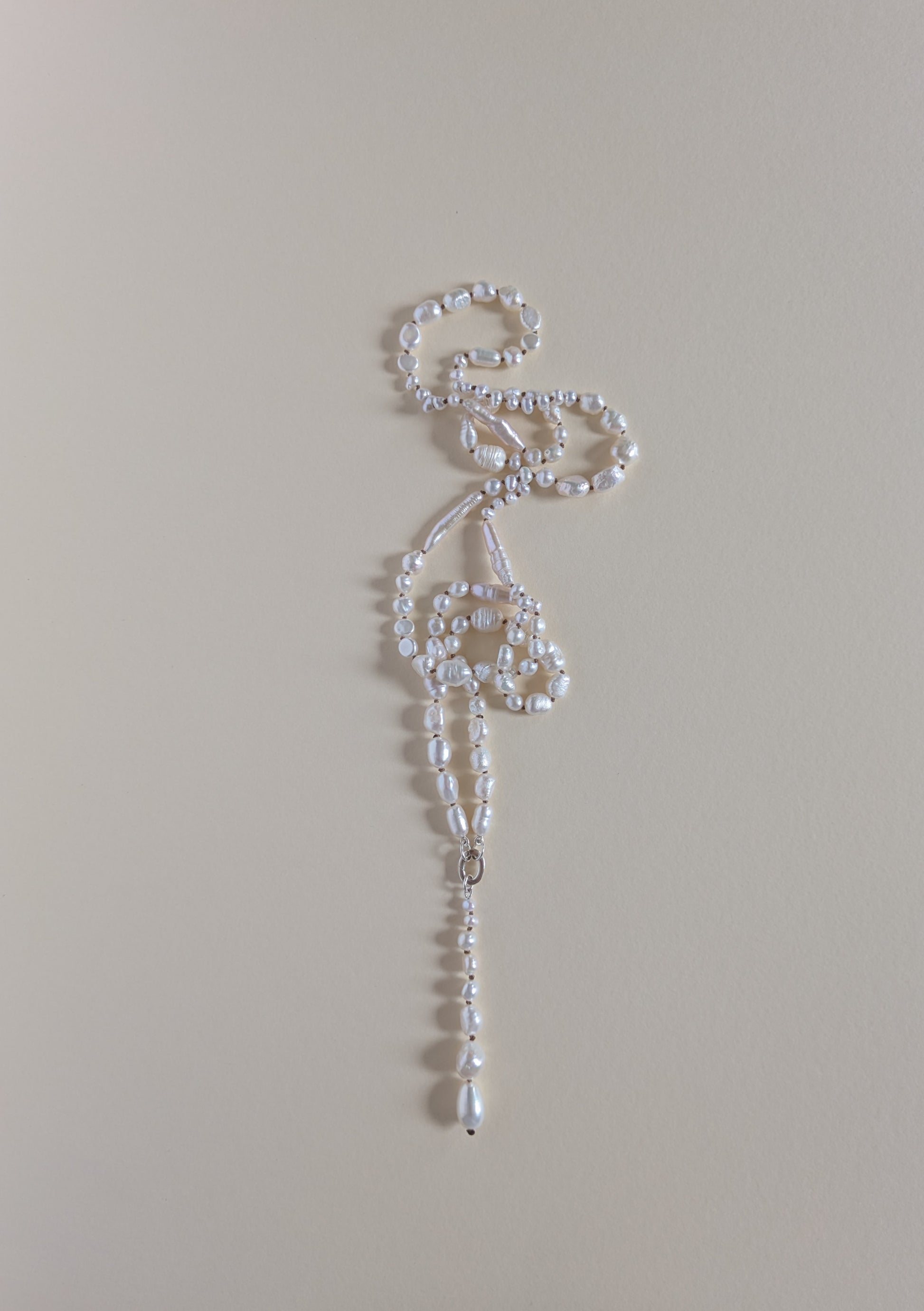 A delicate white beaded necklace with a long, ornate drop pendant, laid flat on a solid beige background.