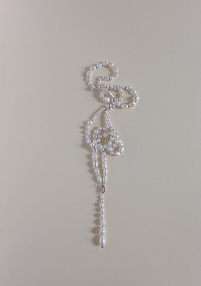 A delicate white beaded necklace with a long, ornate drop pendant, laid flat on a solid beige background.