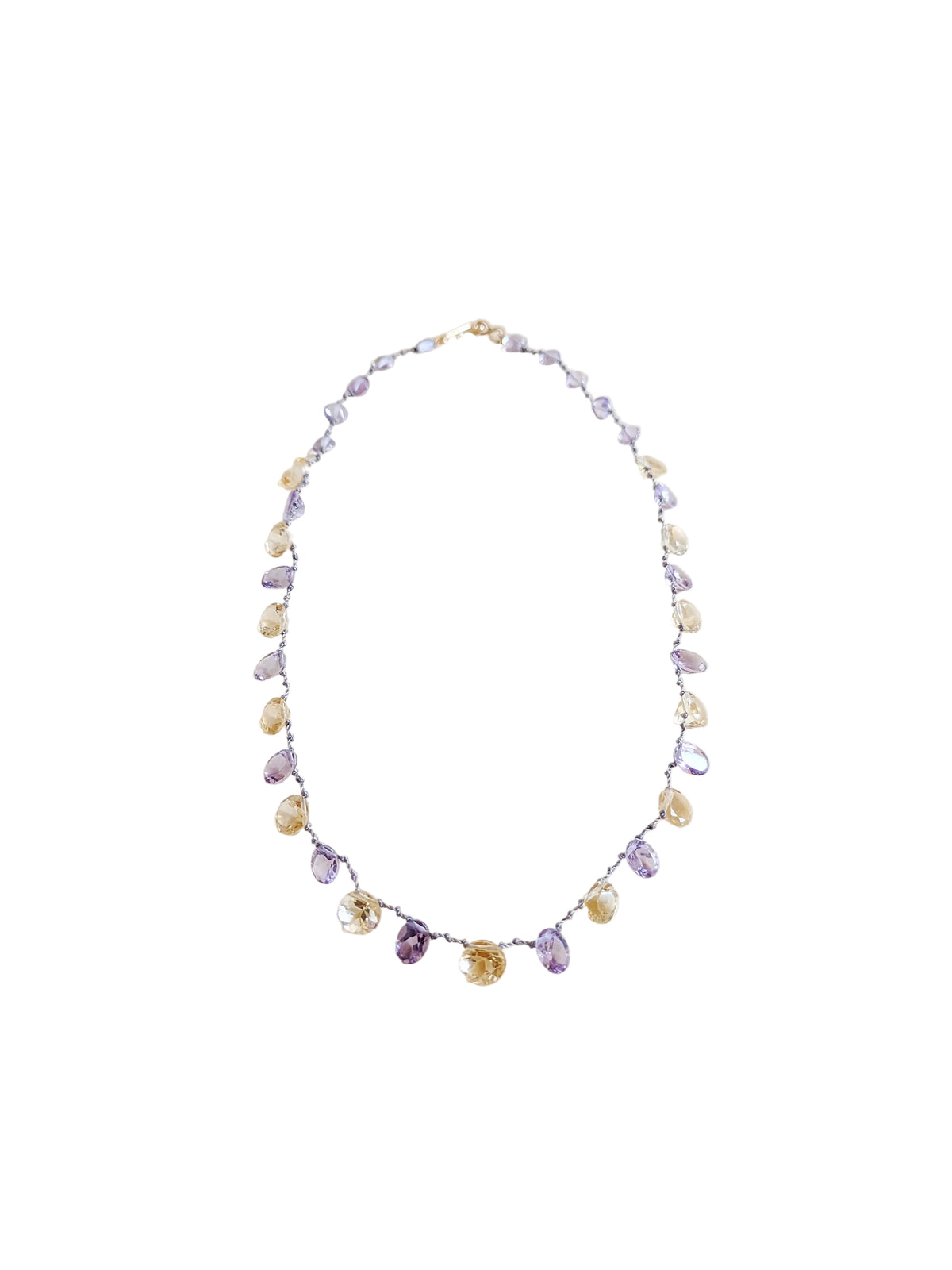 A delicate beaded necklace featuring faceted amethyst and citrine teardrop-shaped gemstones
 on a thin silver wire, laid flat on a warm beige background.