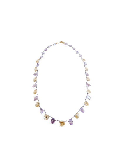 A delicate beaded necklace featuring faceted amethyst and citrine teardrop-shaped gemstones
 on a thin silver wire, laid flat on a warm beige background.