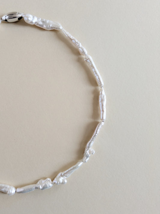 A close-up of a pearl choker made of irregular keshi biwa pearls on a plain beige background.