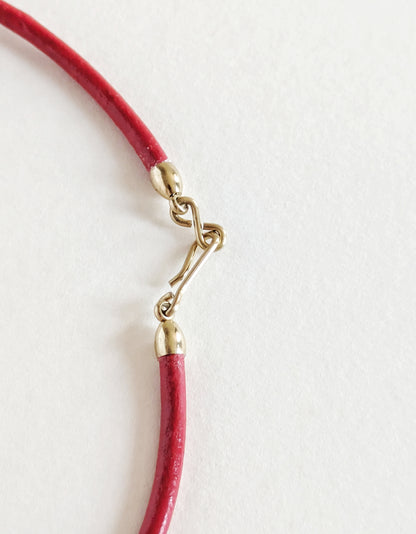Close-up of a red cord with a gold clasp on a light gray background