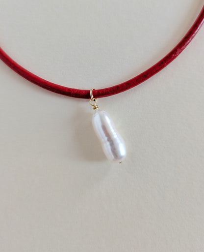 Red choker necklace with a white pearl pendant on a light gray background