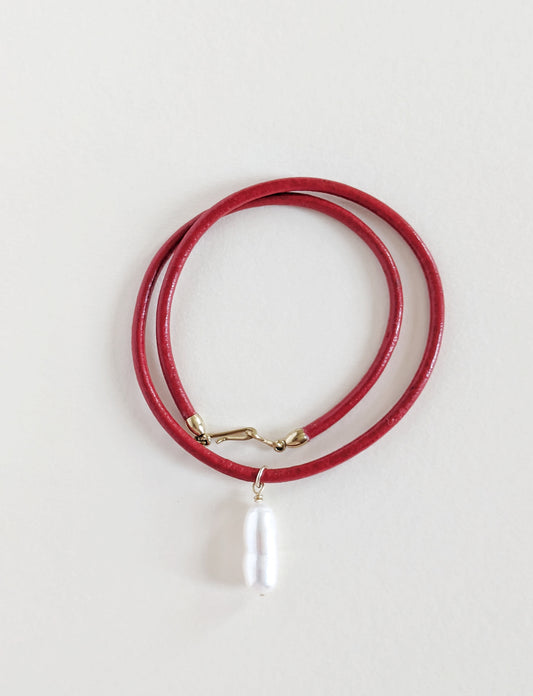 Red leather necklace with a pearl pendant on a light gray background