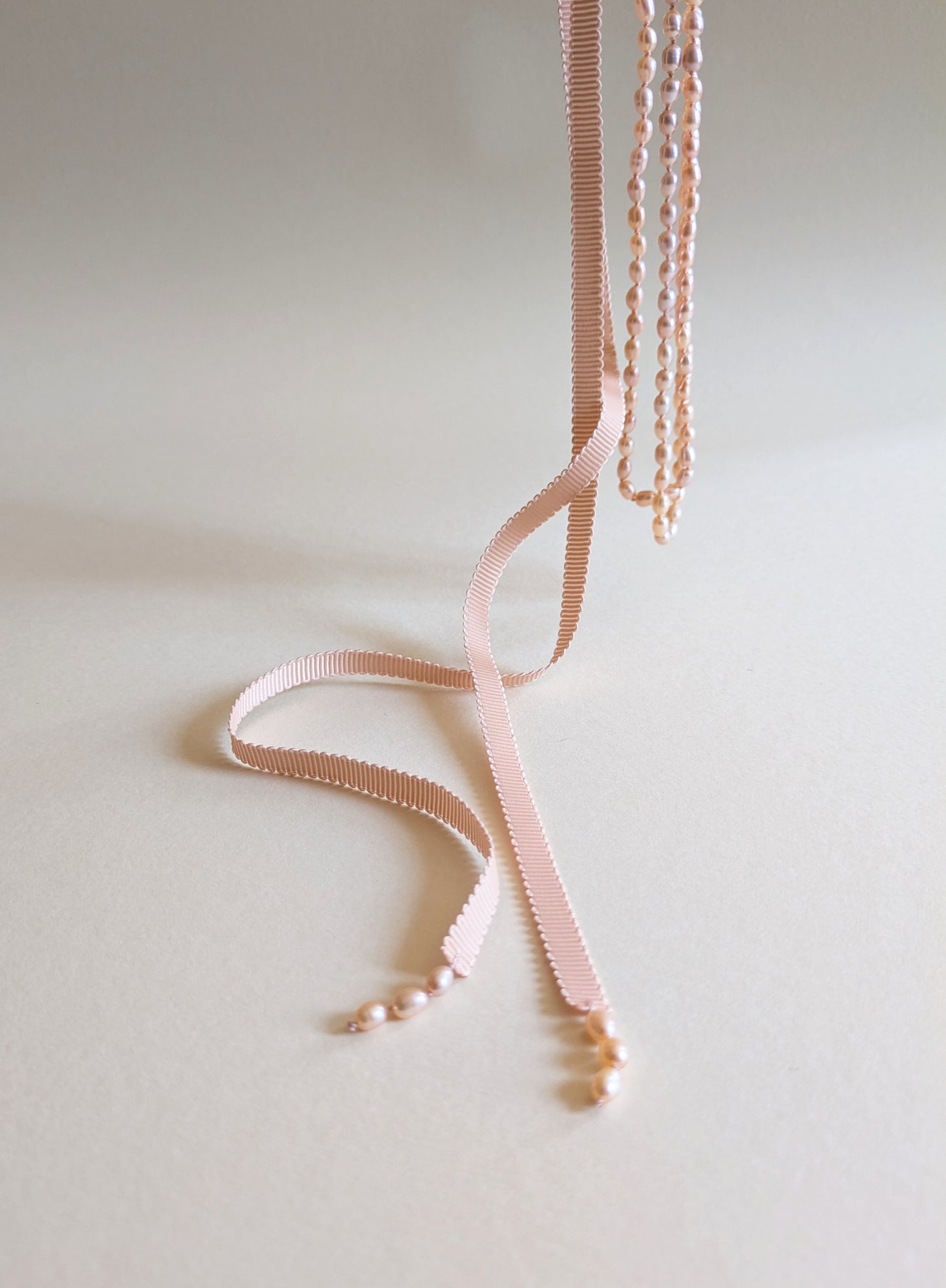 Necklace with pink ribbon and pink pearls on a light background