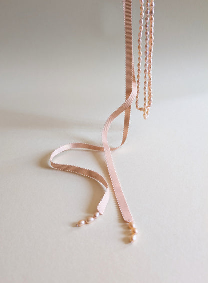 Necklace with pink ribbon and pink pearls on a light background