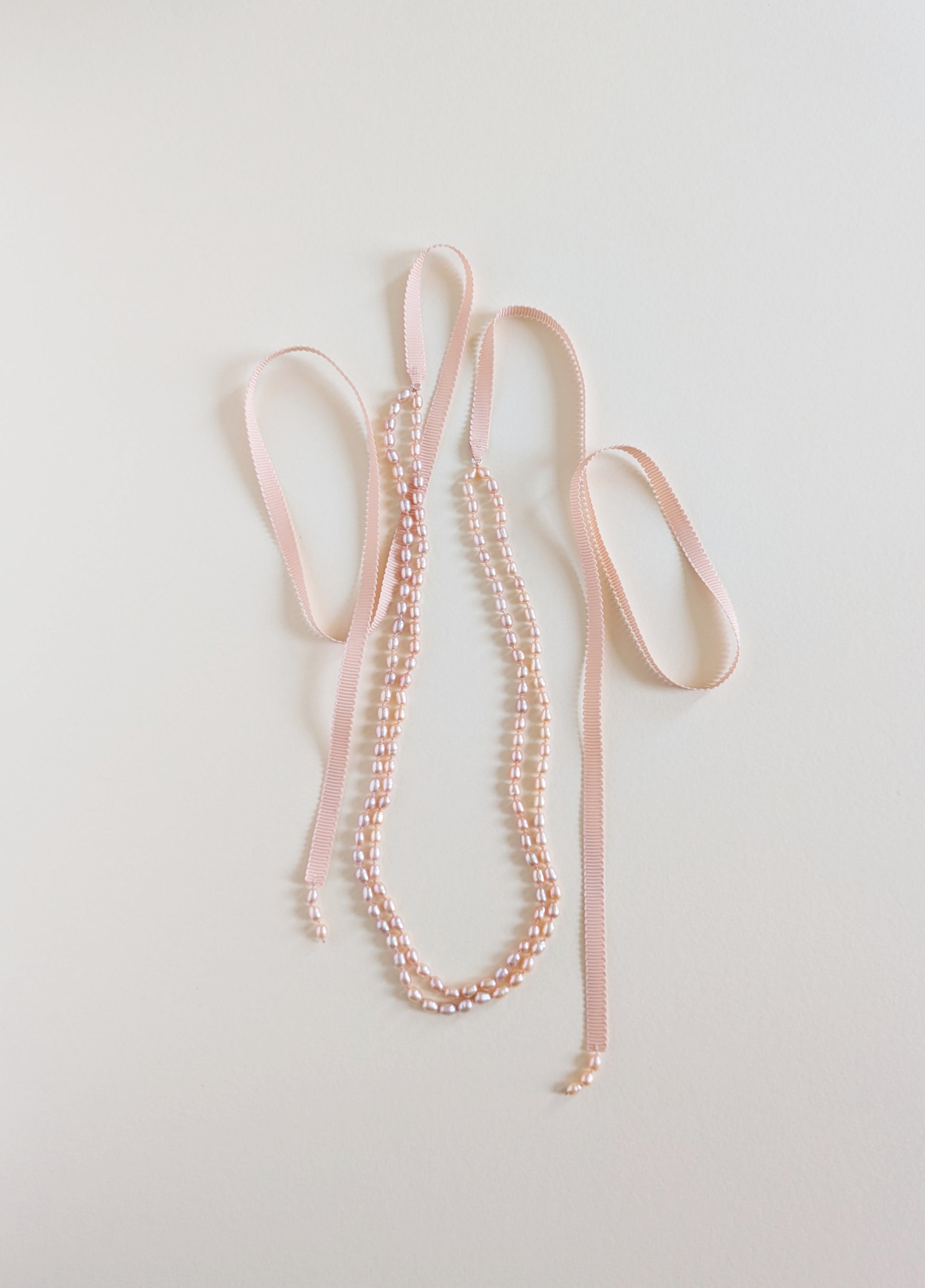Pearl necklace with pink ribbons on a light gray background