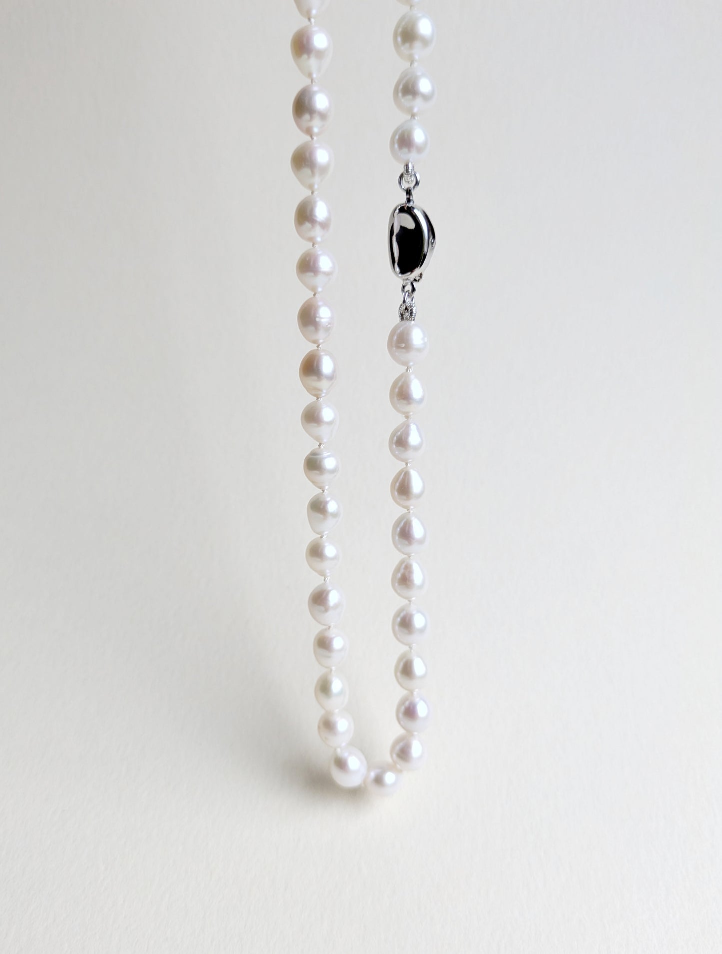Pearl necklace with a silver clasp on a light gray background