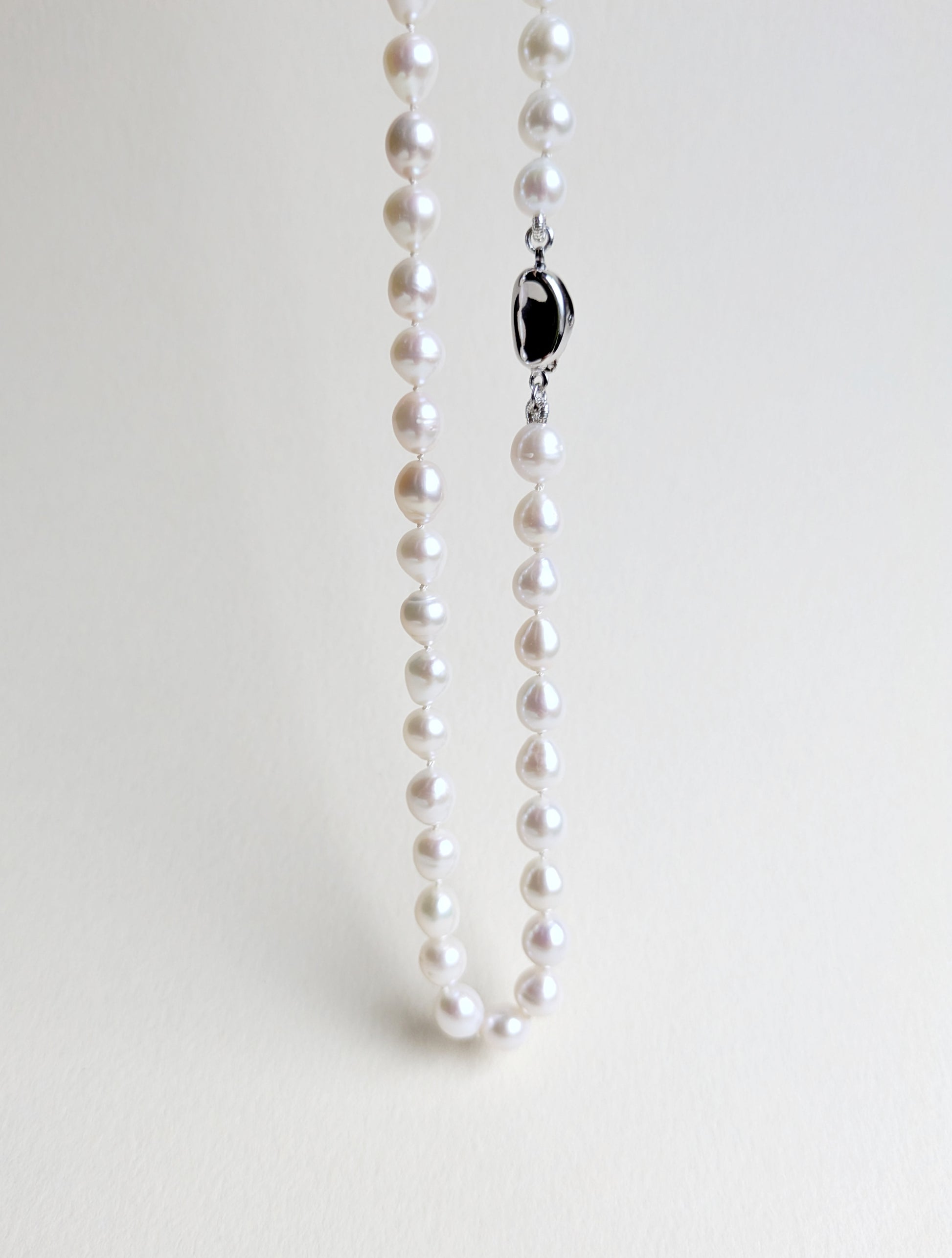 Pearl necklace with a silver clasp on a light gray background