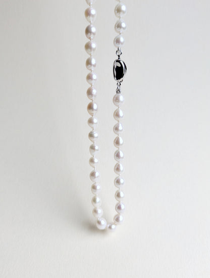 Pearl necklace with a silver clasp on a light gray background