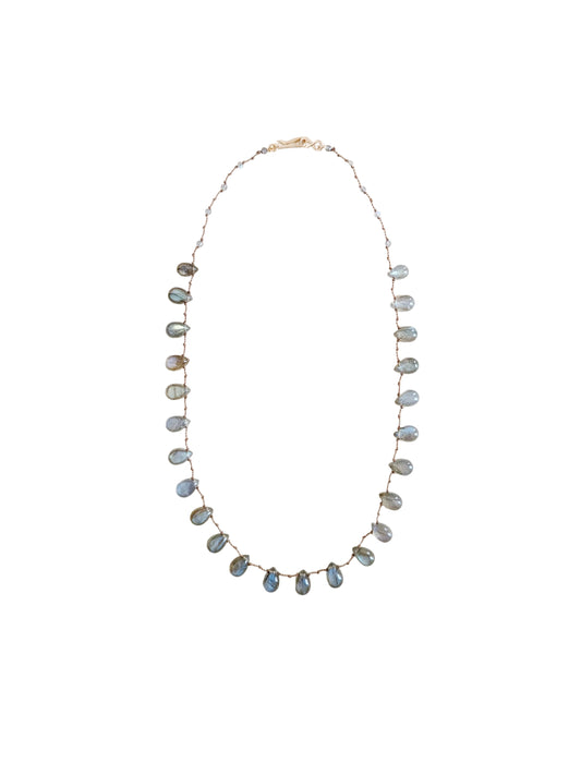 A delicate necklace featuring labradorite teardrop beads against a  solid off-white background.