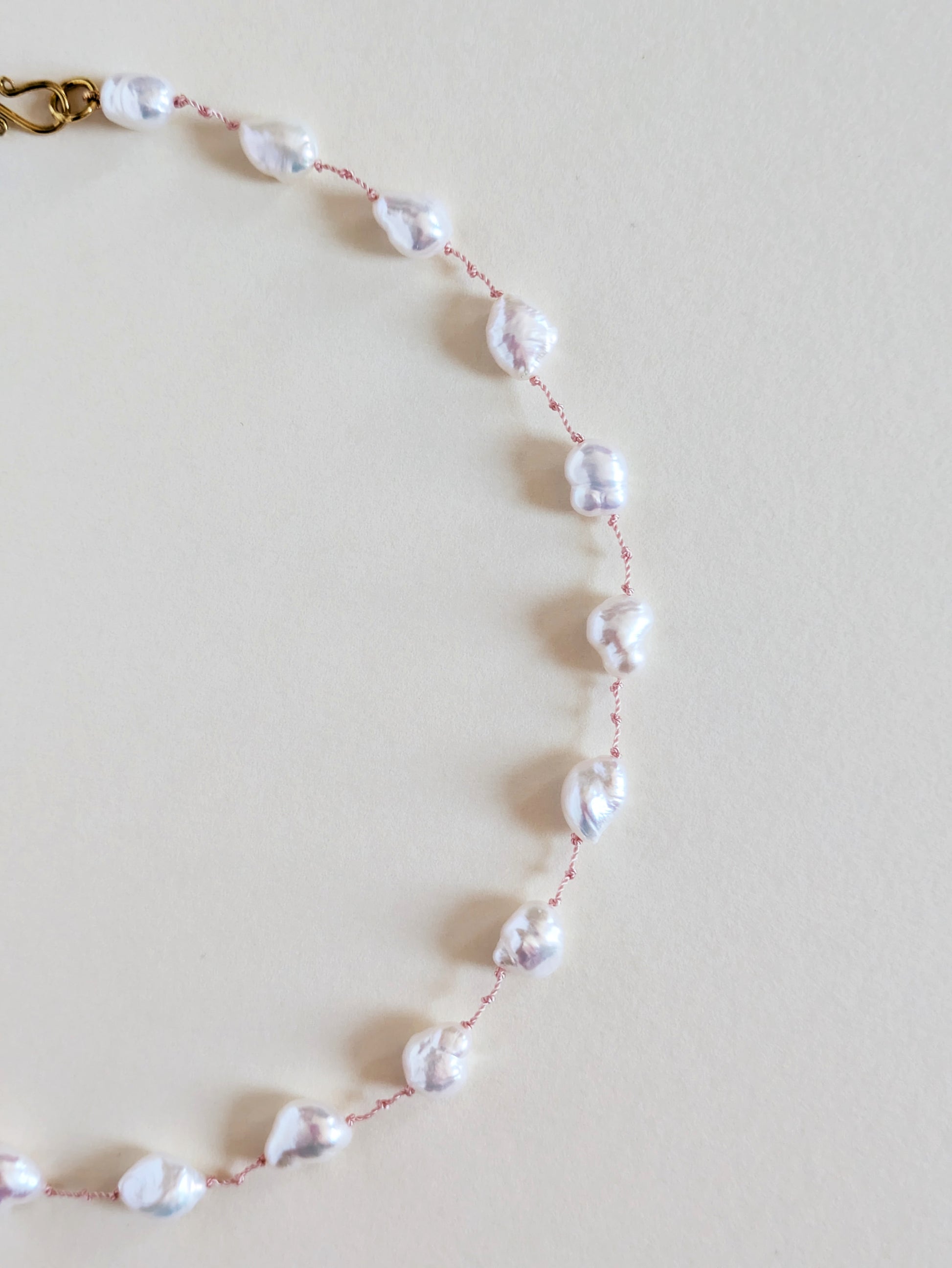 Details of pearl necklace with gold clasp on a light beige background.