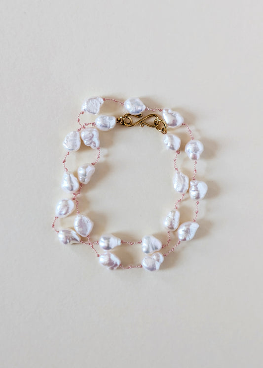 Pearl necklace with gold clasp on a white background.