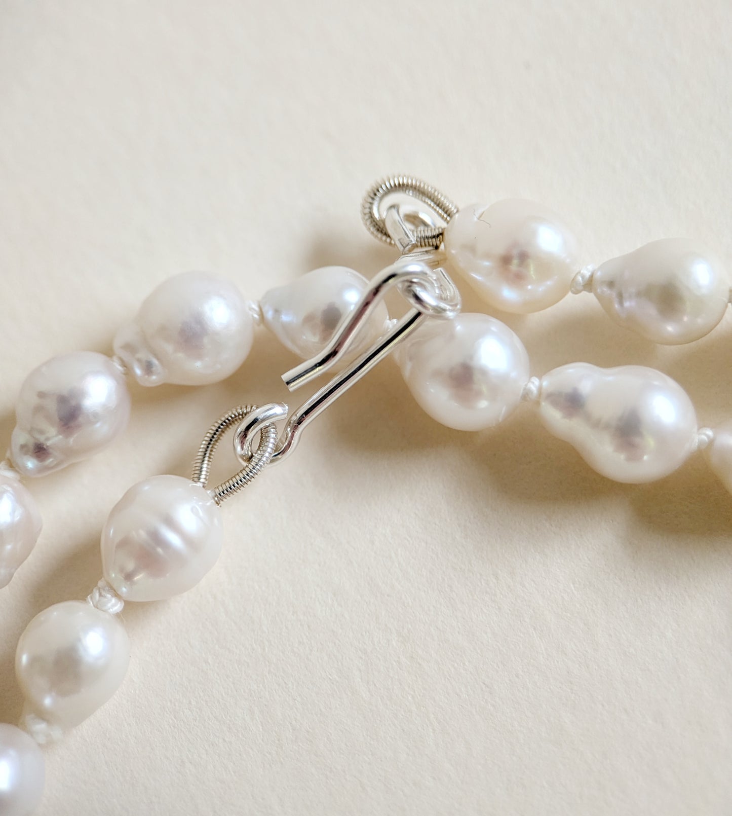 Pearl necklace with silver clasp on a light beige background
