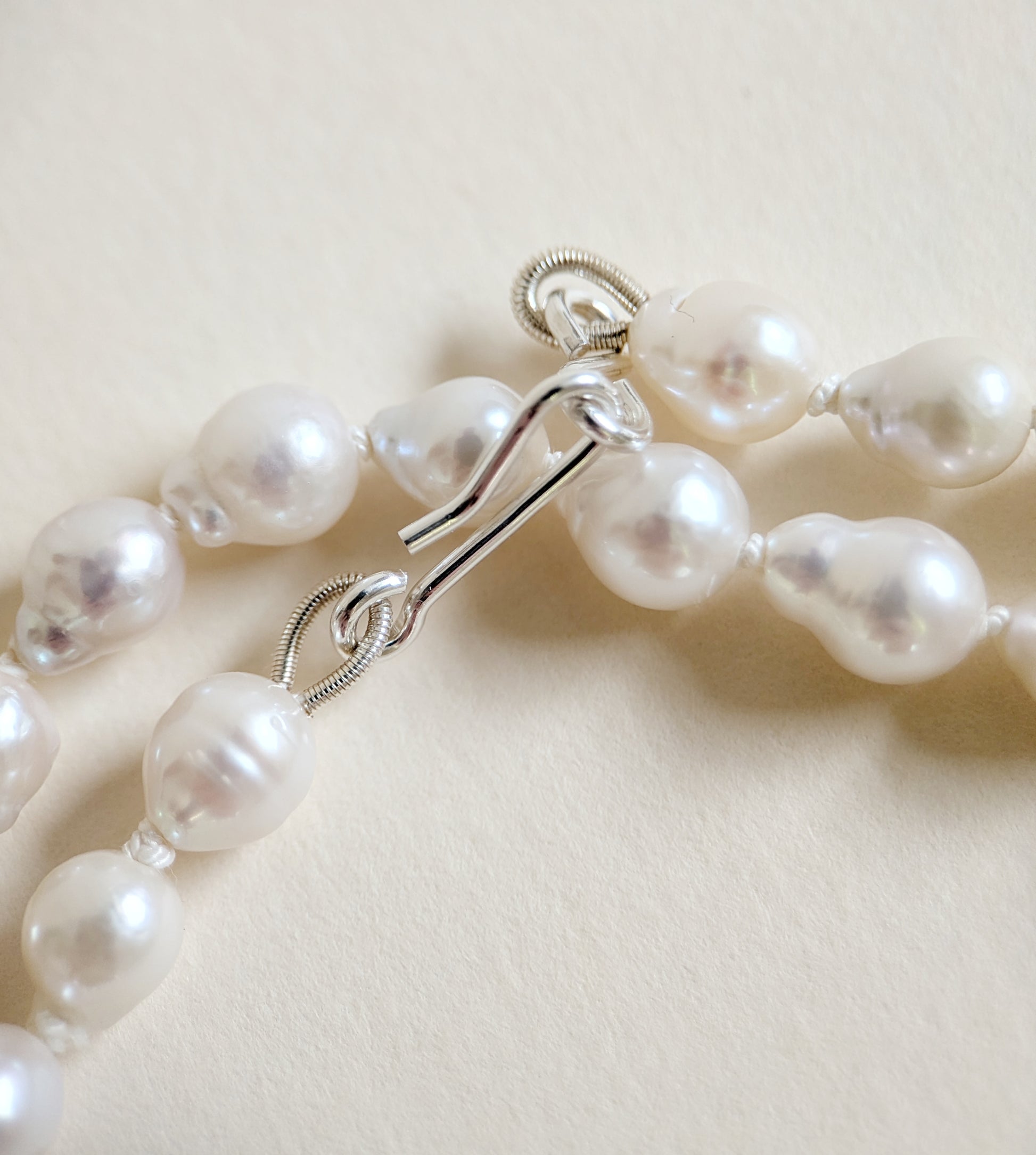 Pearl necklace with silver clasp on a light beige background