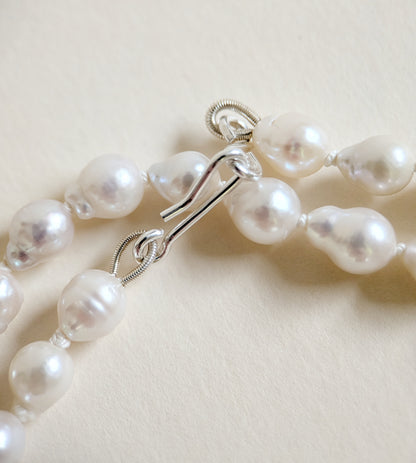 Pearl necklace with silver clasp on a light beige background