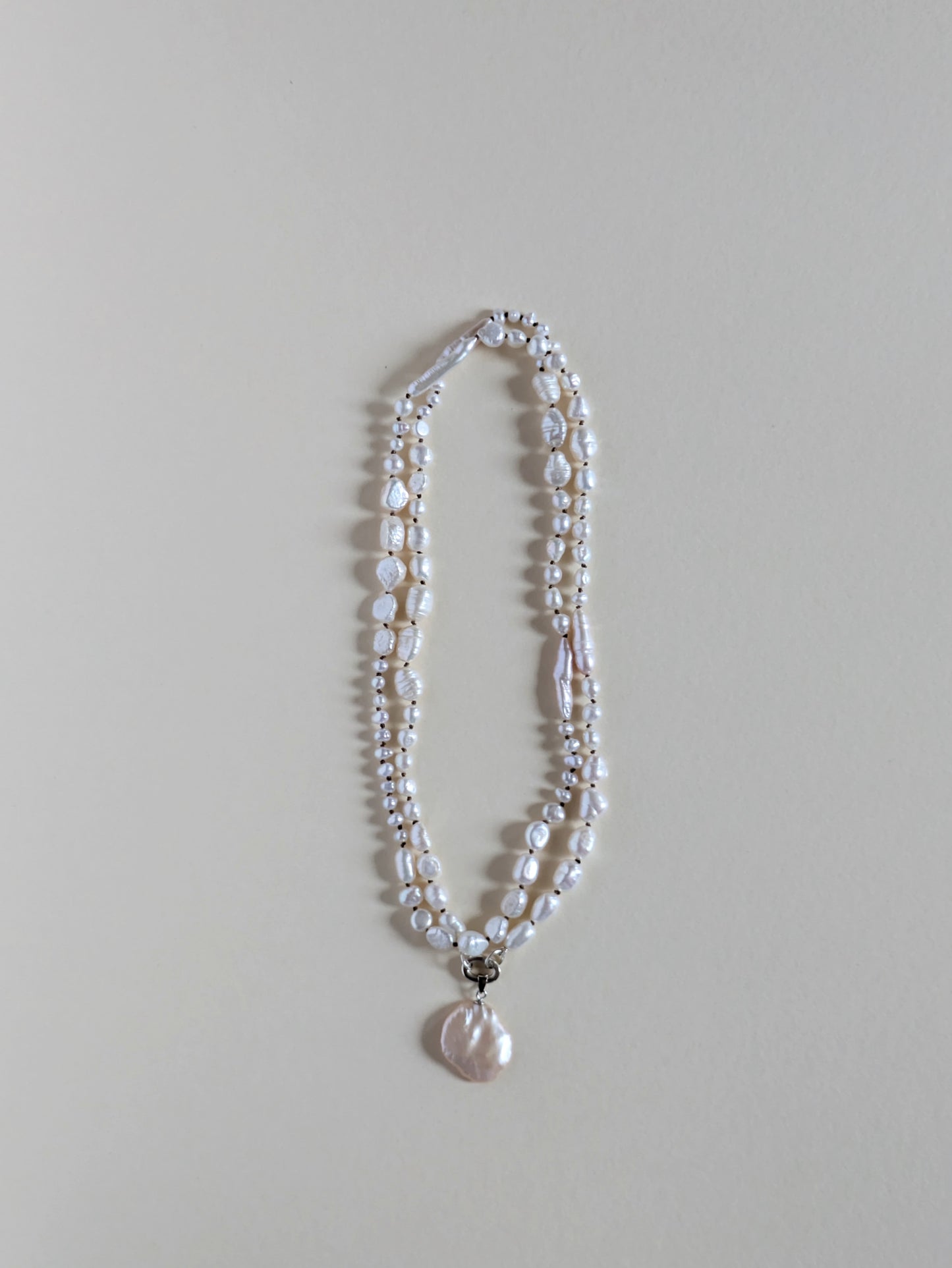 Two strand long pearl necklace with a pendant on a silver clasp.