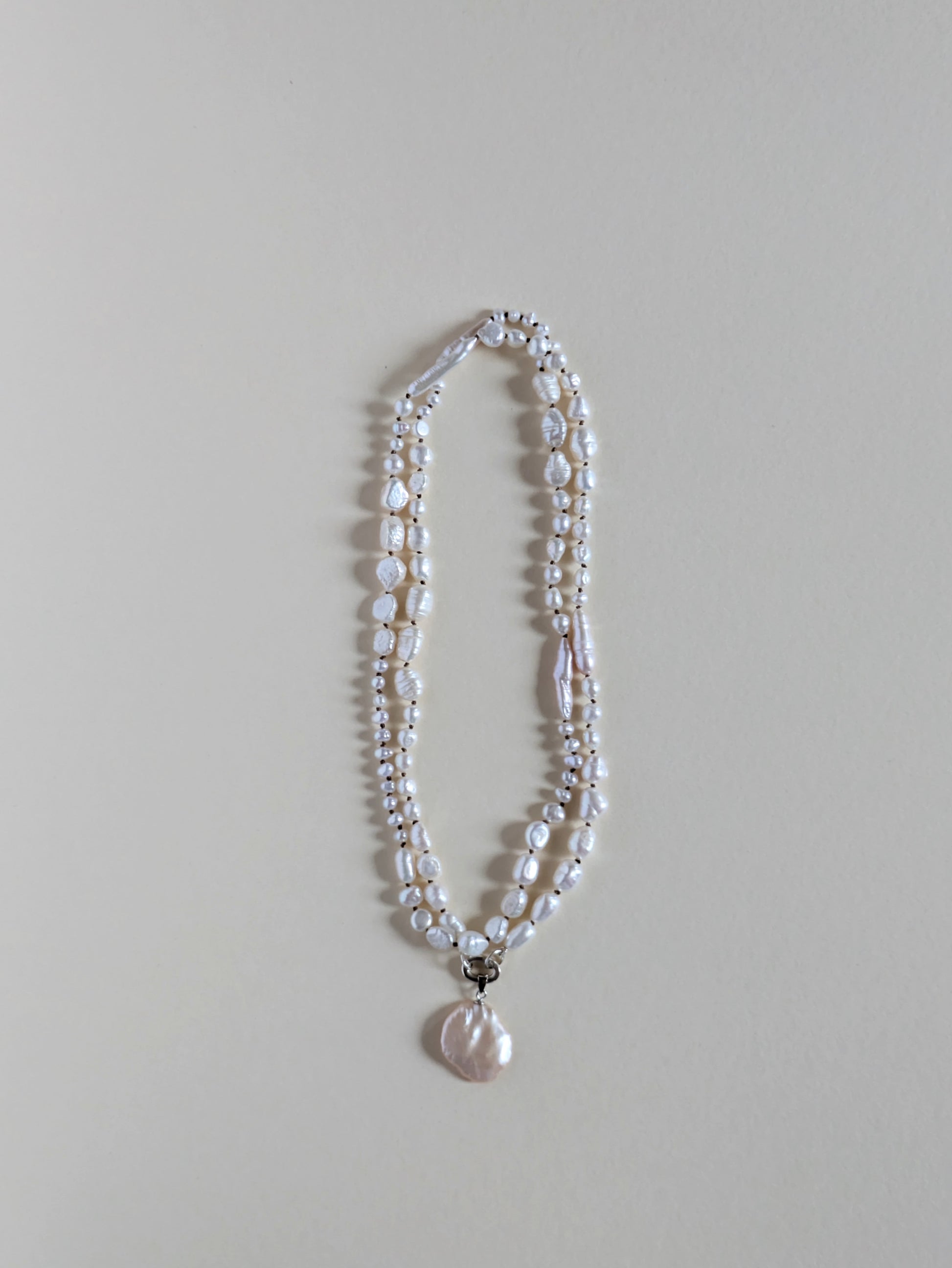 Two strand long pearl necklace with a pendant on a silver clasp.