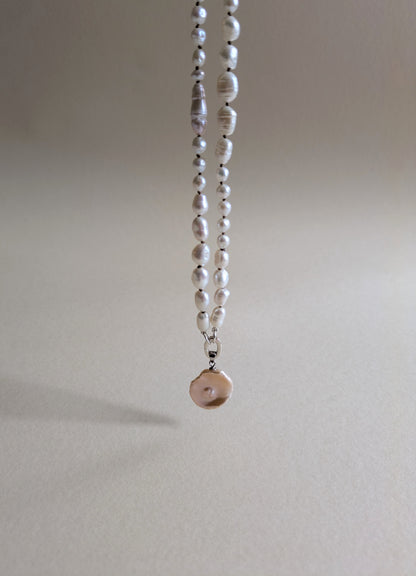 Pearl necklace with a pendant on a plain background