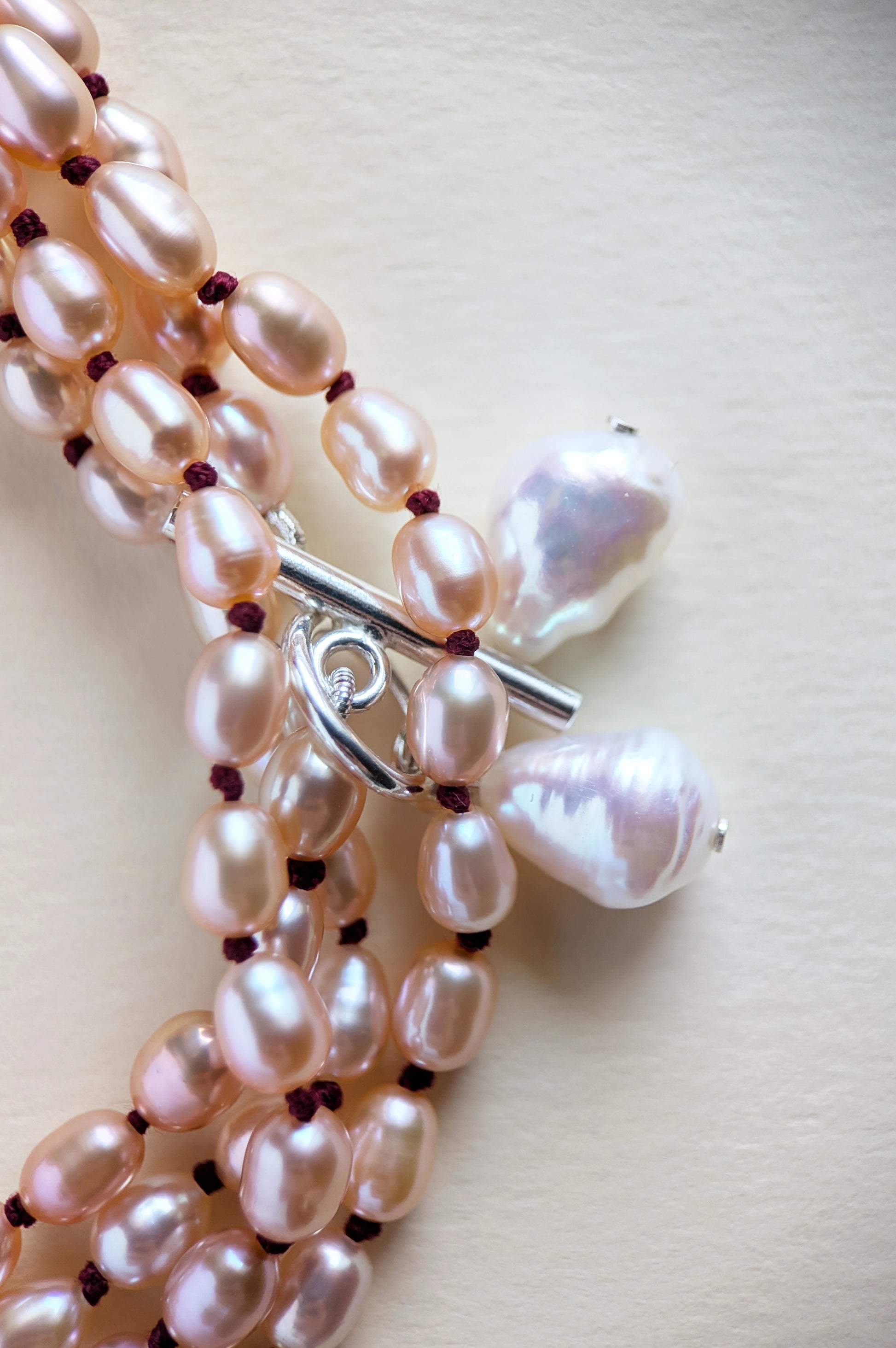 Details of a long pink rice pearl necklace on a light beige background.
