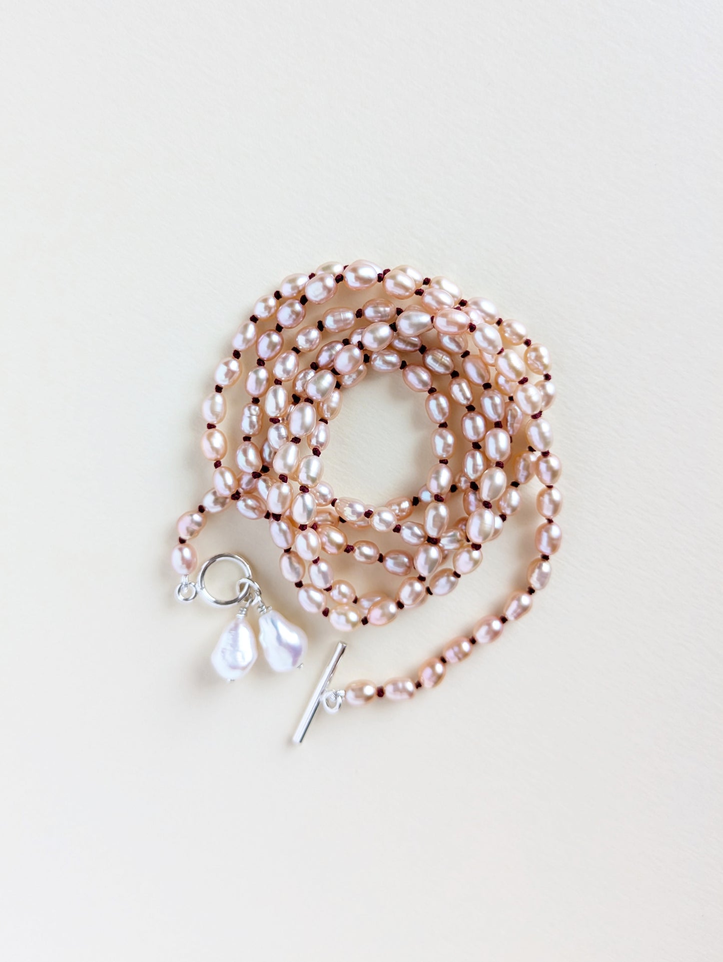 Details of a long pink rice pearl necklace with silver clasp.