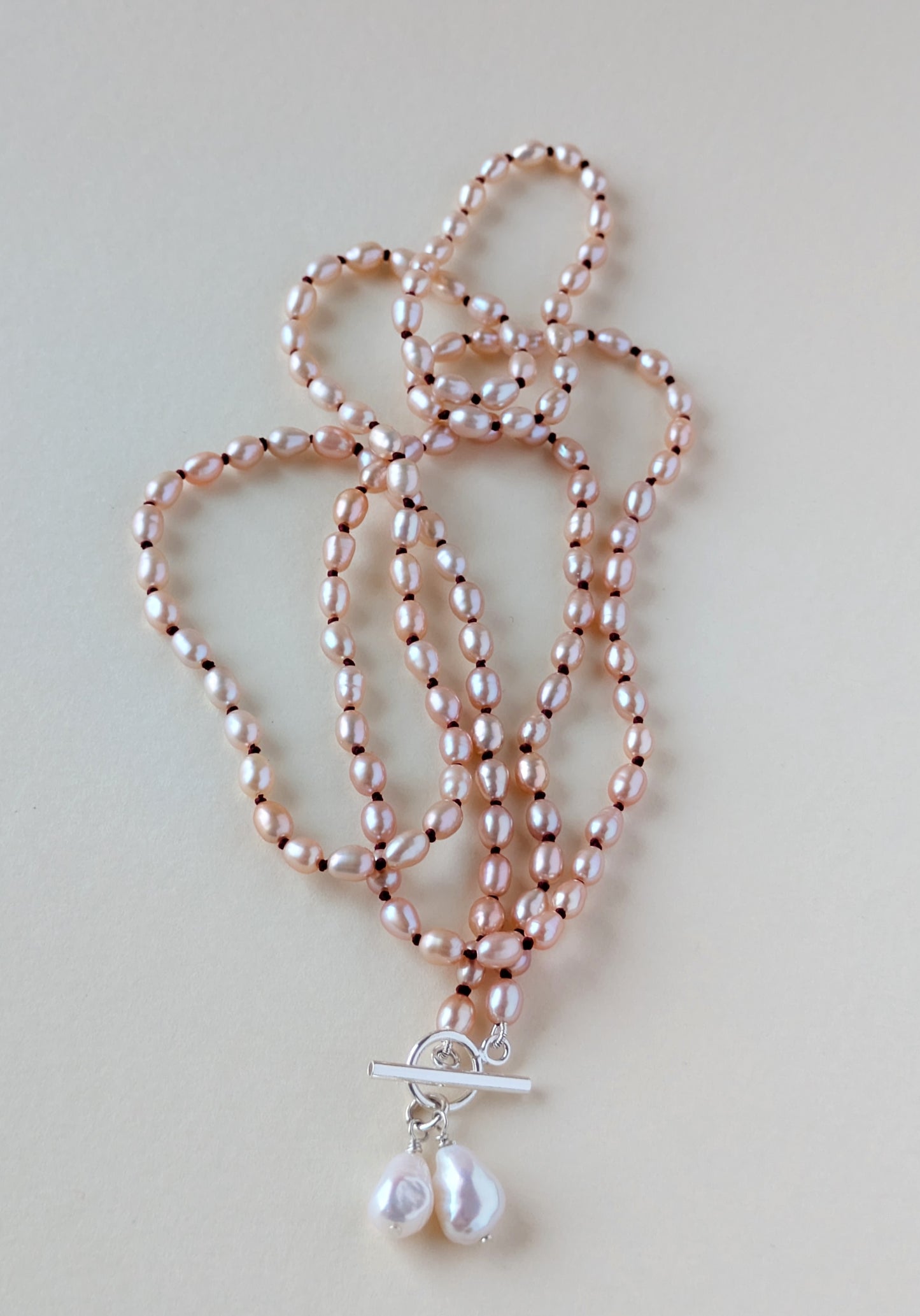 Long pink rice pearl necklace with a pendant ona silver clasp.