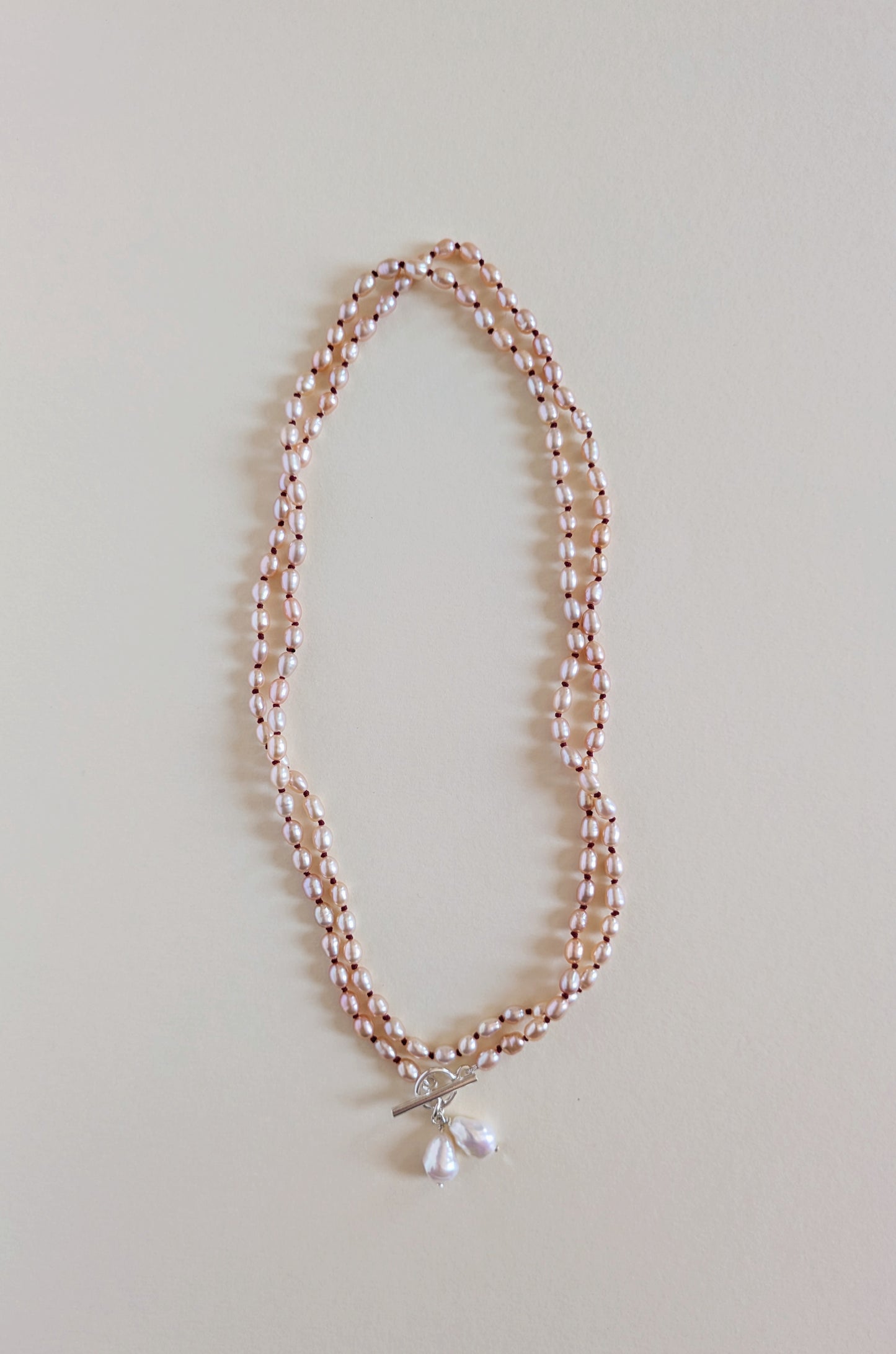 Two strands of a long pink rice pearl necklace with a pendant.