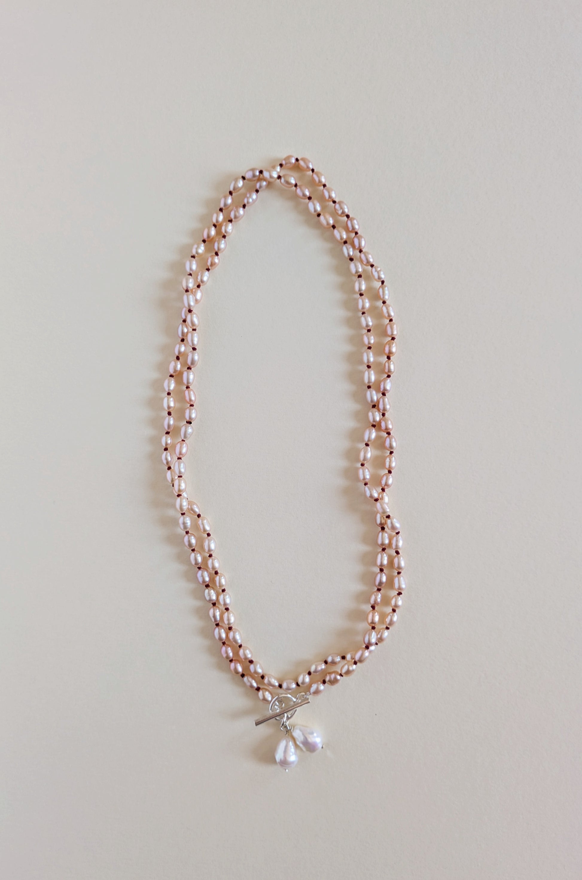 Two strands of a long pink rice pearl necklace with a pendant.