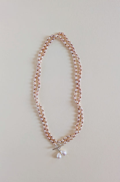 Two strands of a long pink rice pearl necklace with a pendant.
