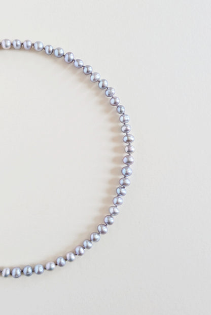 Silver grey pearl necklace on a light beige background