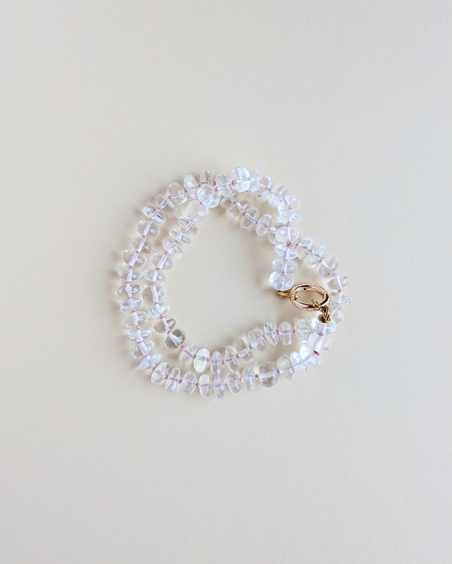 A delicate beaded bracelet made of clear faceted beads with a small gold clasp, photographed on a plain light beige background.