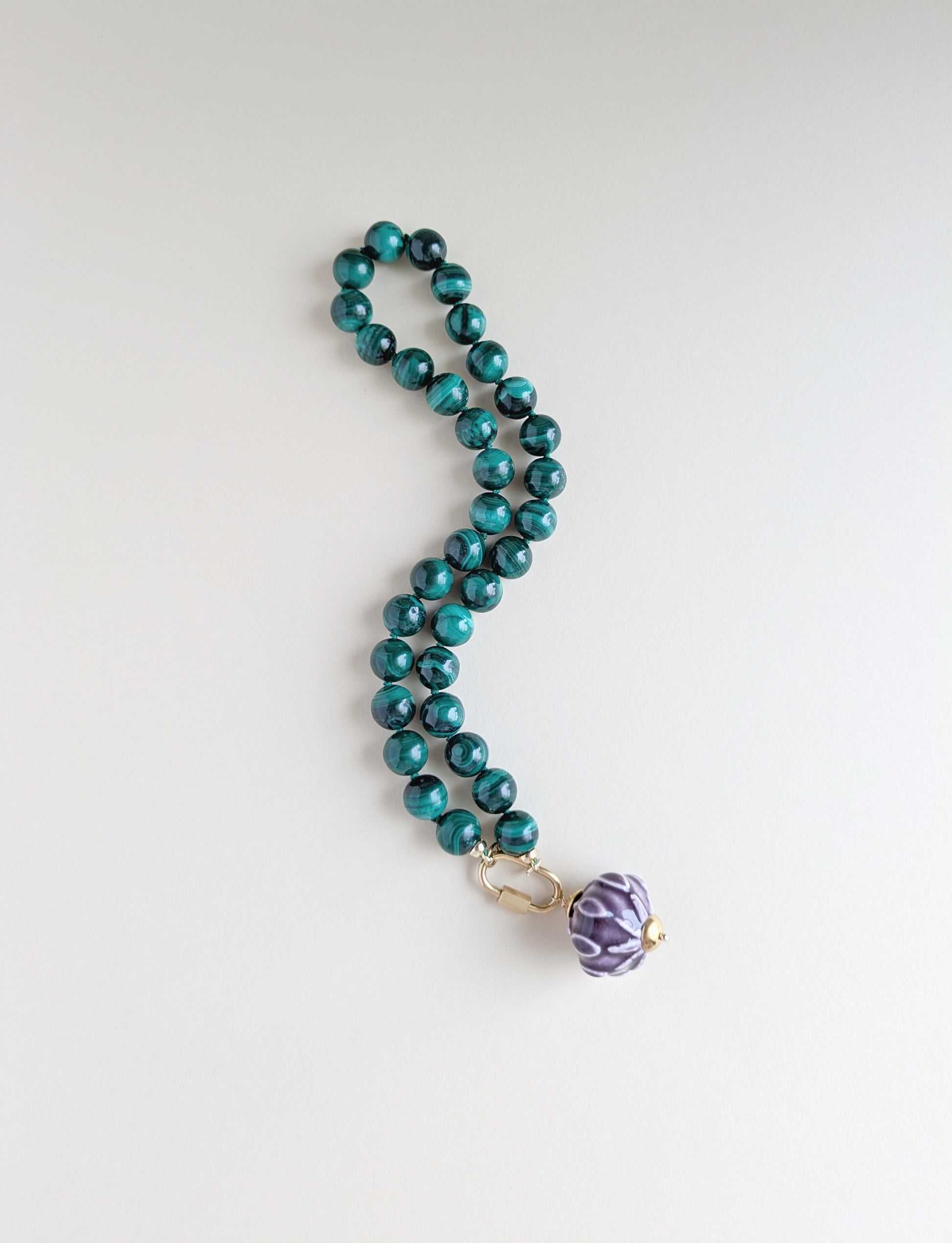 A beaded necklace with glossy malachite beads and a purple patterned pendant, displayed on a clean white background.