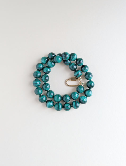 A beaded strand bracelet made of glossy malachite beads with a small gold clasp, photographed on a clean white background.