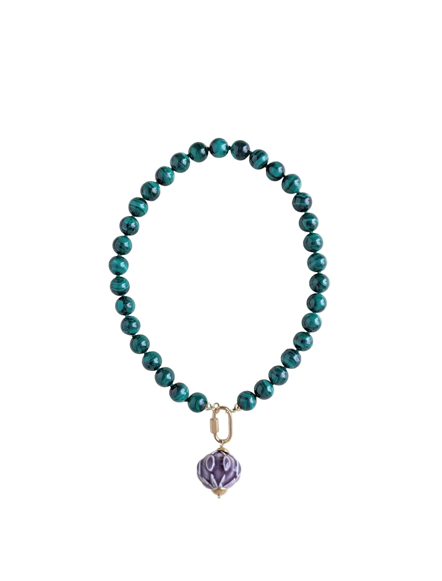 A beaded necklace with glossy malachite beads and a small purple faceted pendant, photographed on a plain light background.