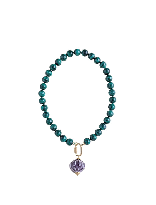 A beaded necklace with glossy malachite beads and a small purple faceted pendant, photographed on a plain light background.