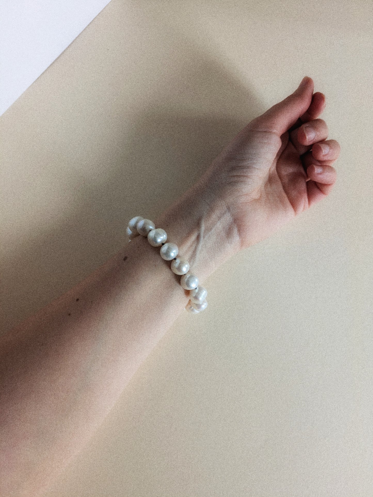 Hand wearing a pearl bracelet on a plain background