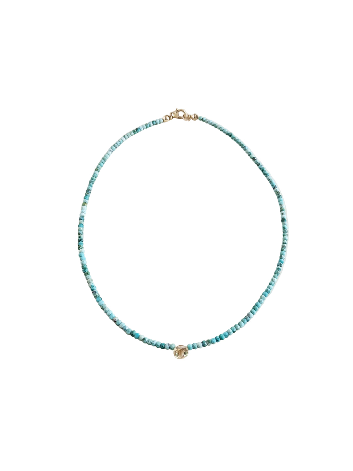 A delicate beaded necklace with small turquoise-blue beads and gold-toned hardware, displayed on a clean, light beige background.