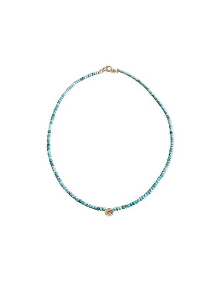 A delicate beaded necklace with small turquoise-blue beads and gold-toned hardware, displayed on a clean, light beige background.