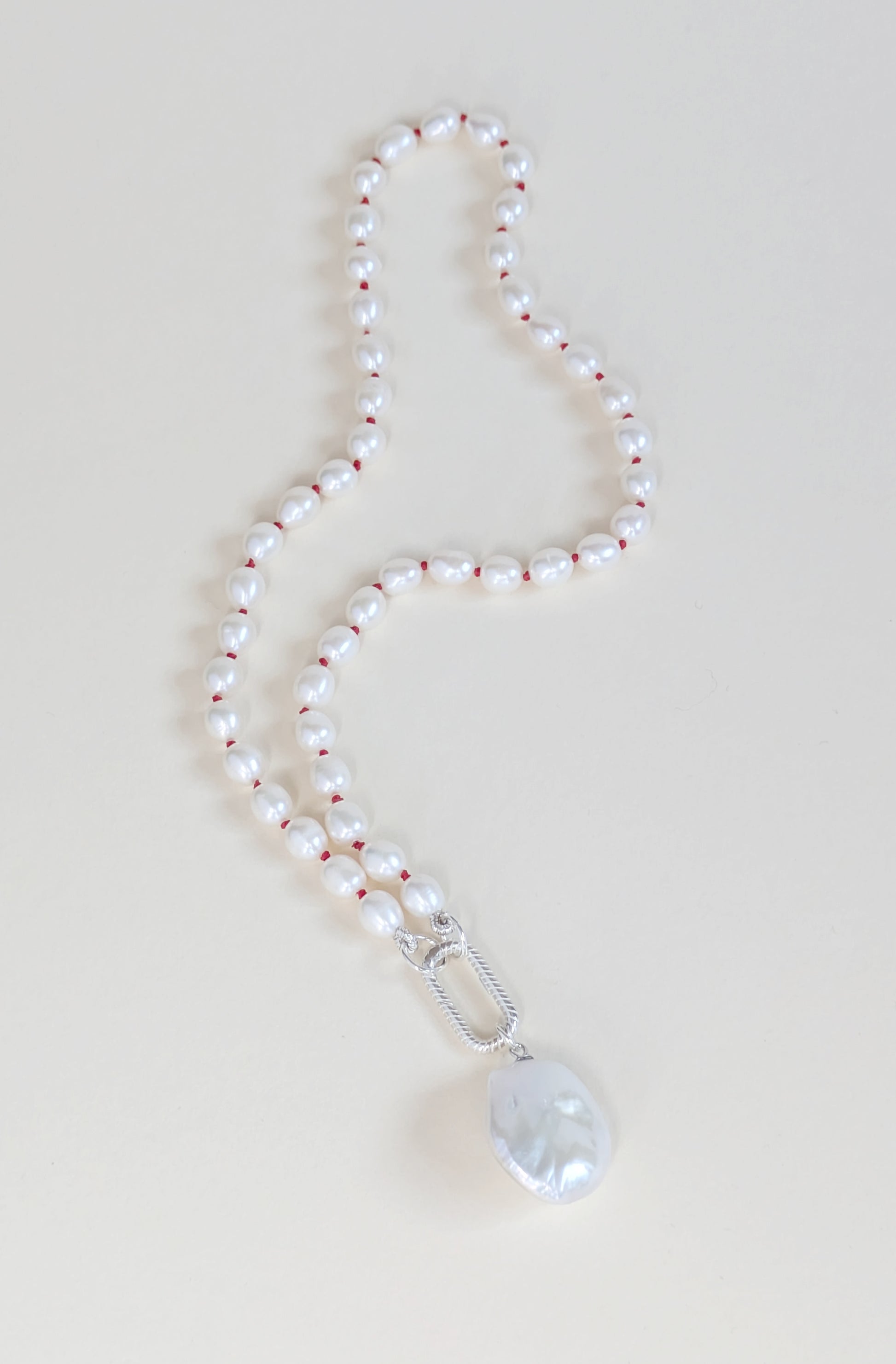 Pearl necklace with a silver clasp and pendant on a light background