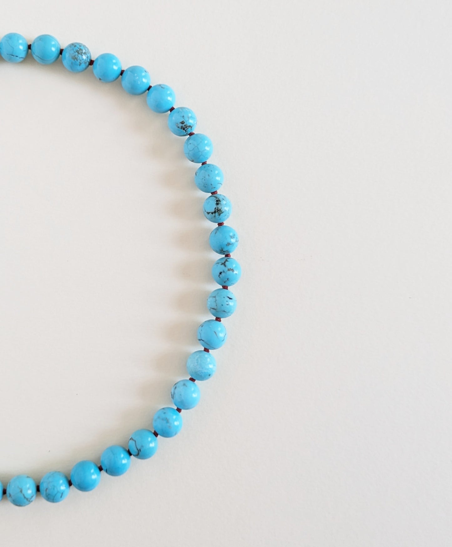 Turquoise necklace Oasis details on a beige background.