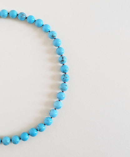 Turquoise necklace Oasis details on a beige background.